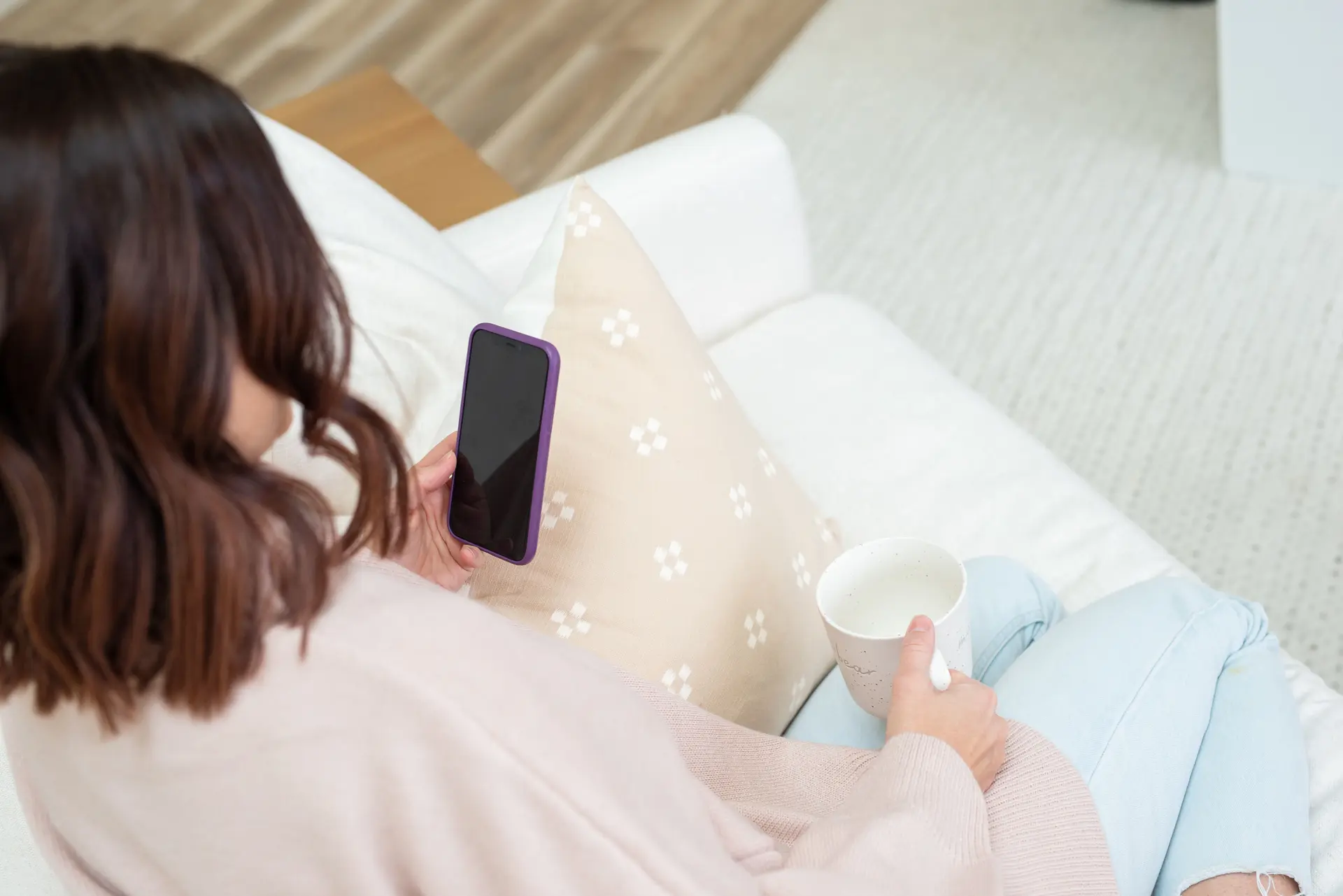 A mom on the couch with her phone and a cup of coffee